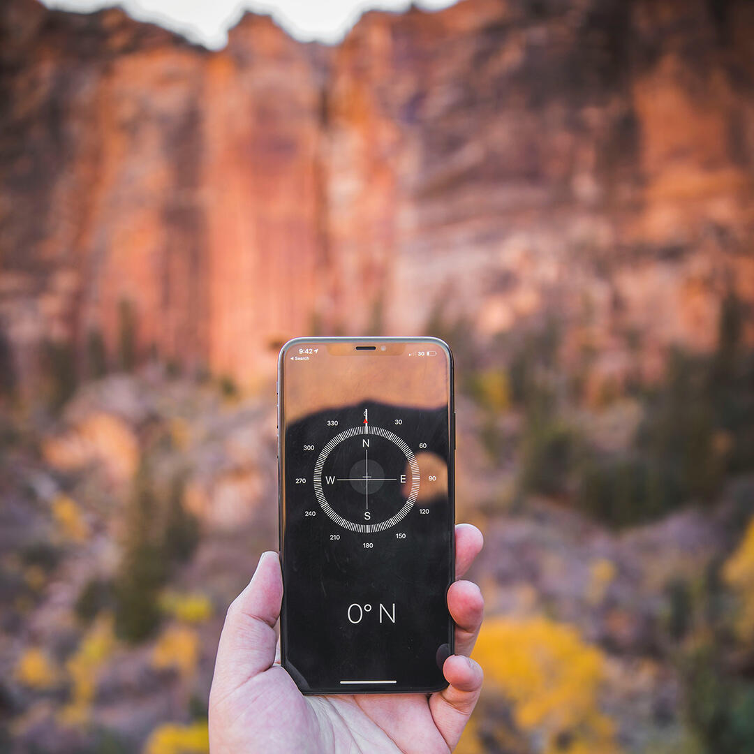 Mann hält Handy mit Kompass-App in der Hand, im Hintergrund ist eine Berglandschaft zu sehen