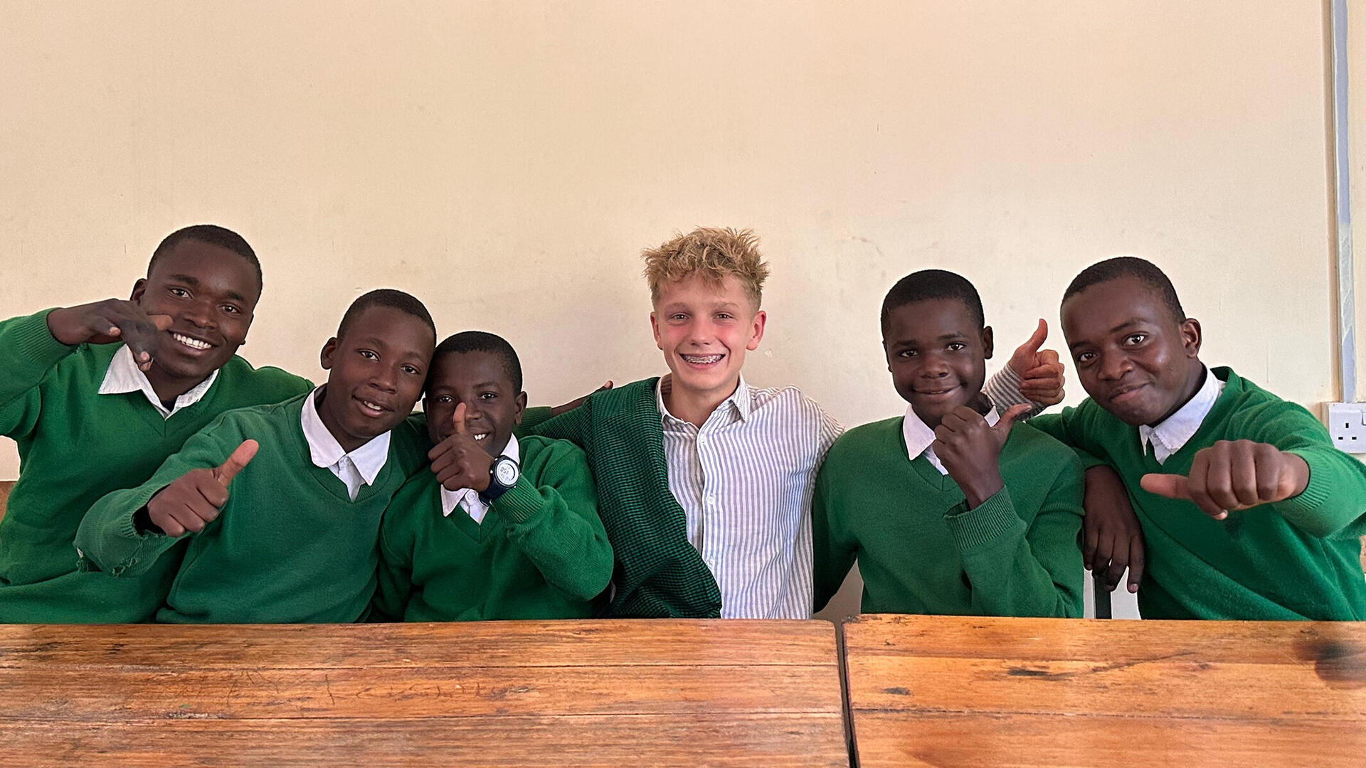 Ein bayerischer Schüler sitzt umringt von fünf tansanischen Schülern an einem Tisch.