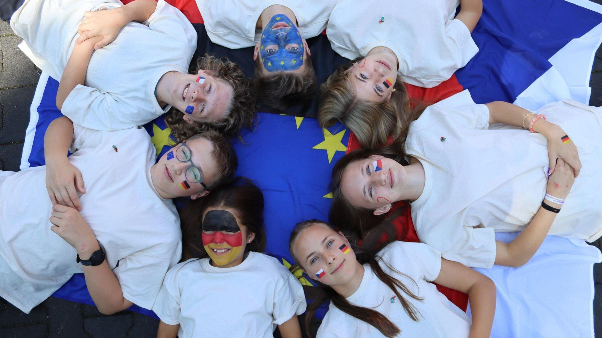Mit Flaggen aus Europa geschminkte Jugendliche liegen im Kreis