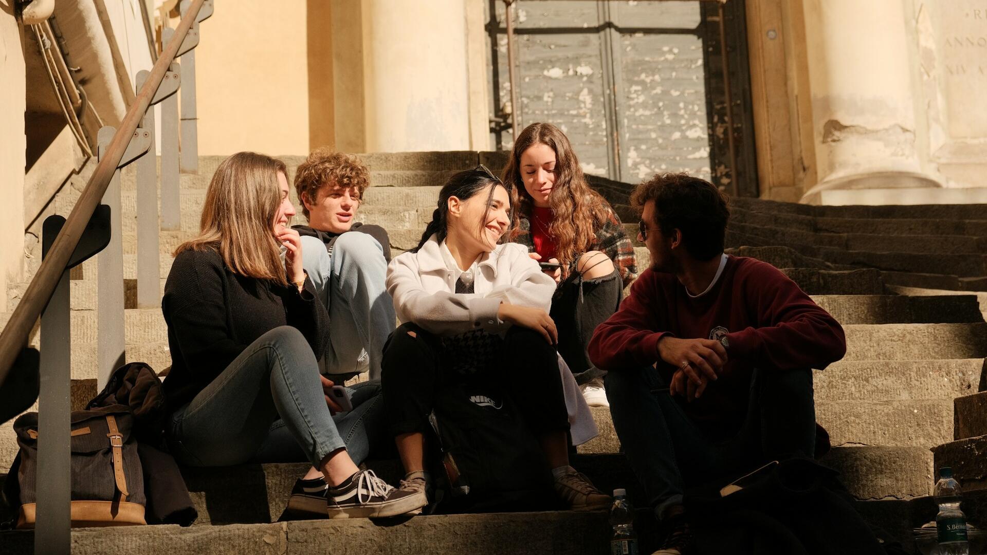 Eine Gruppe junger Menschen sitzt auf einer Treppe vor einem Gebäude.