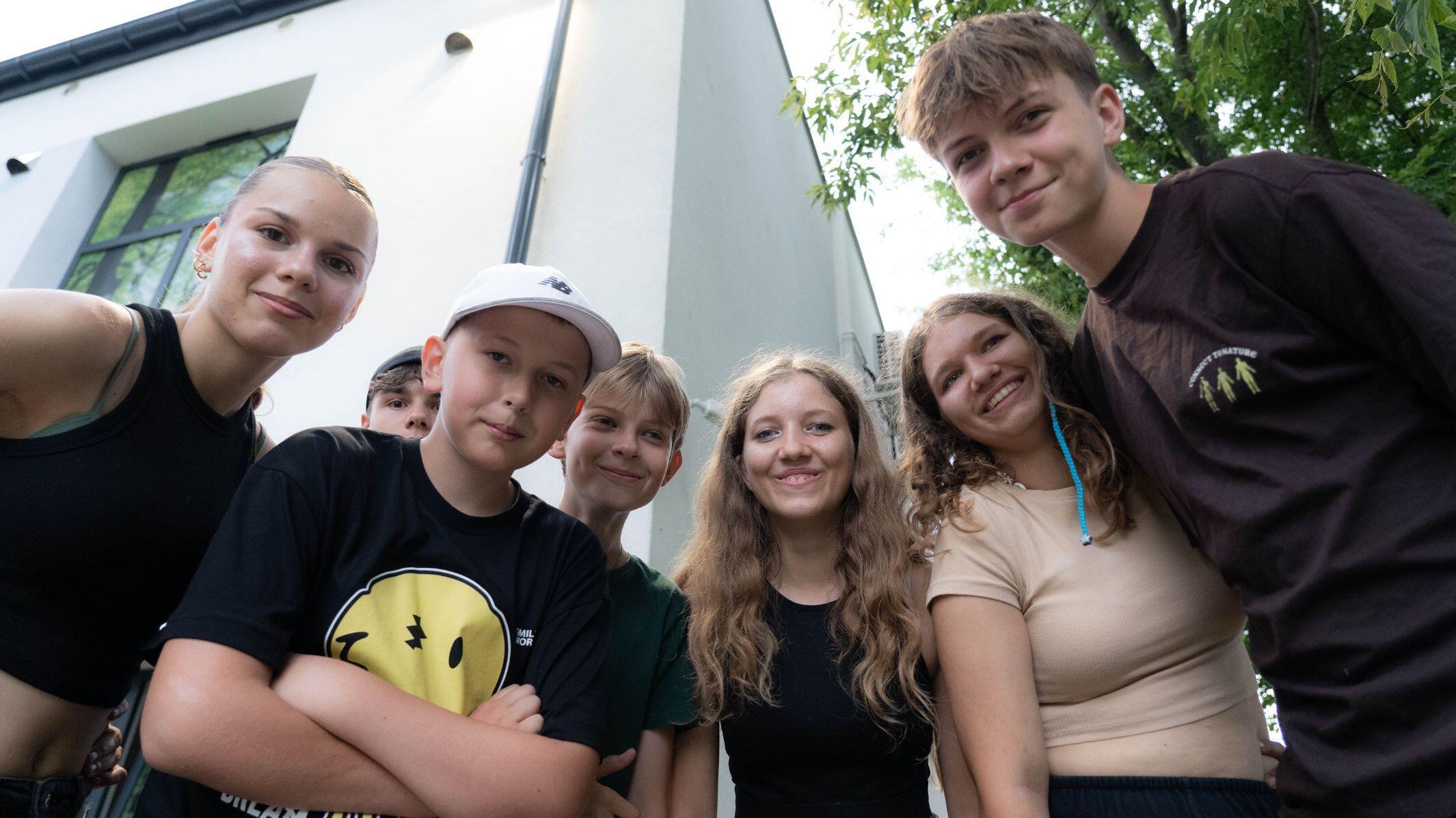 Sieben junge Menschen gucken fröhlich in die Kamera