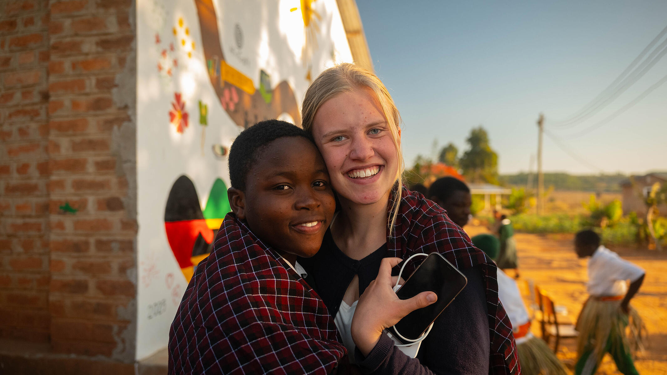 Tansanische und deutsche Schülerin umarmen sich vor der bemalten Wand.