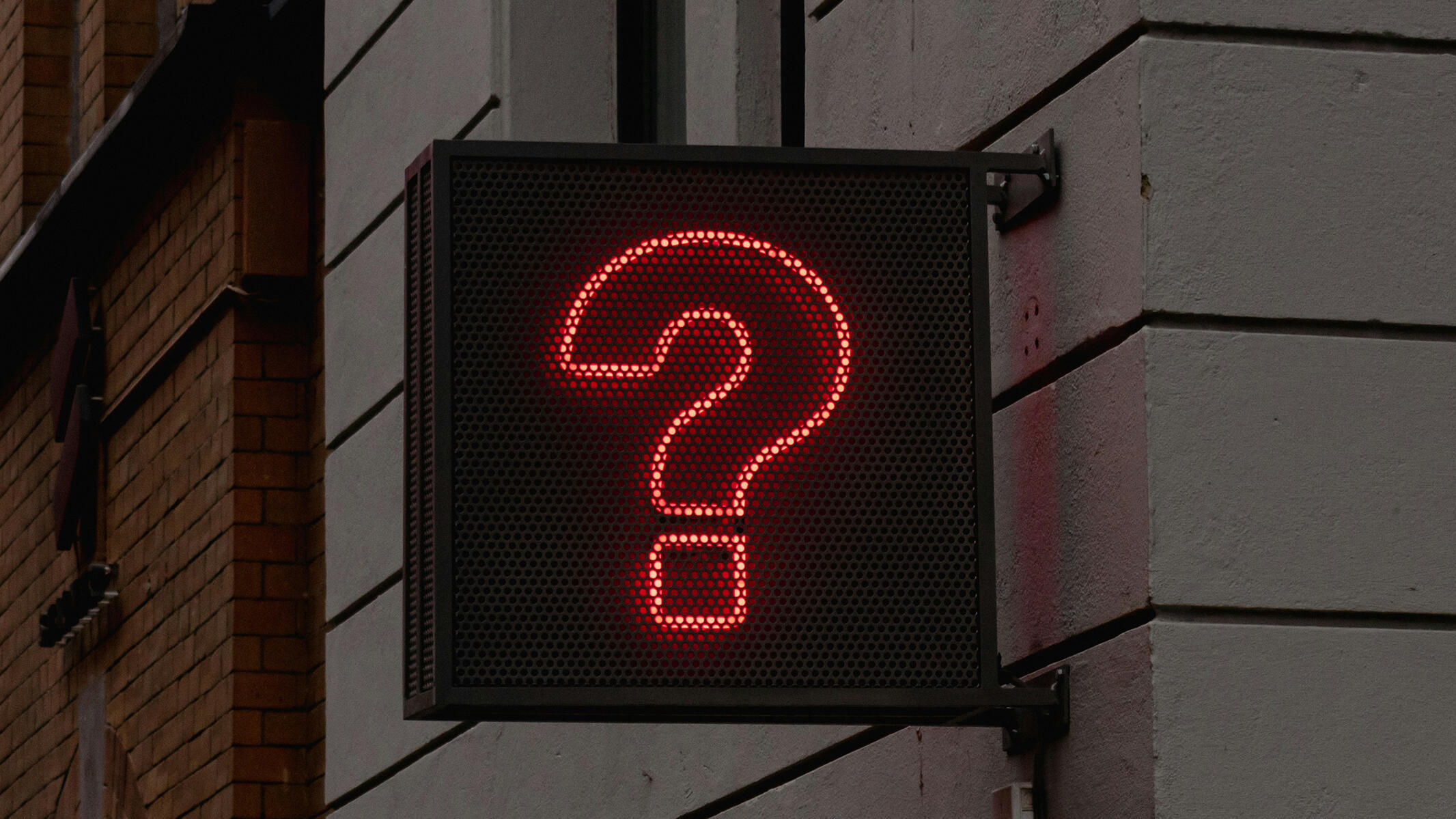 Leuchtzeichen mit rotem Fragezeichen an Häuserwand