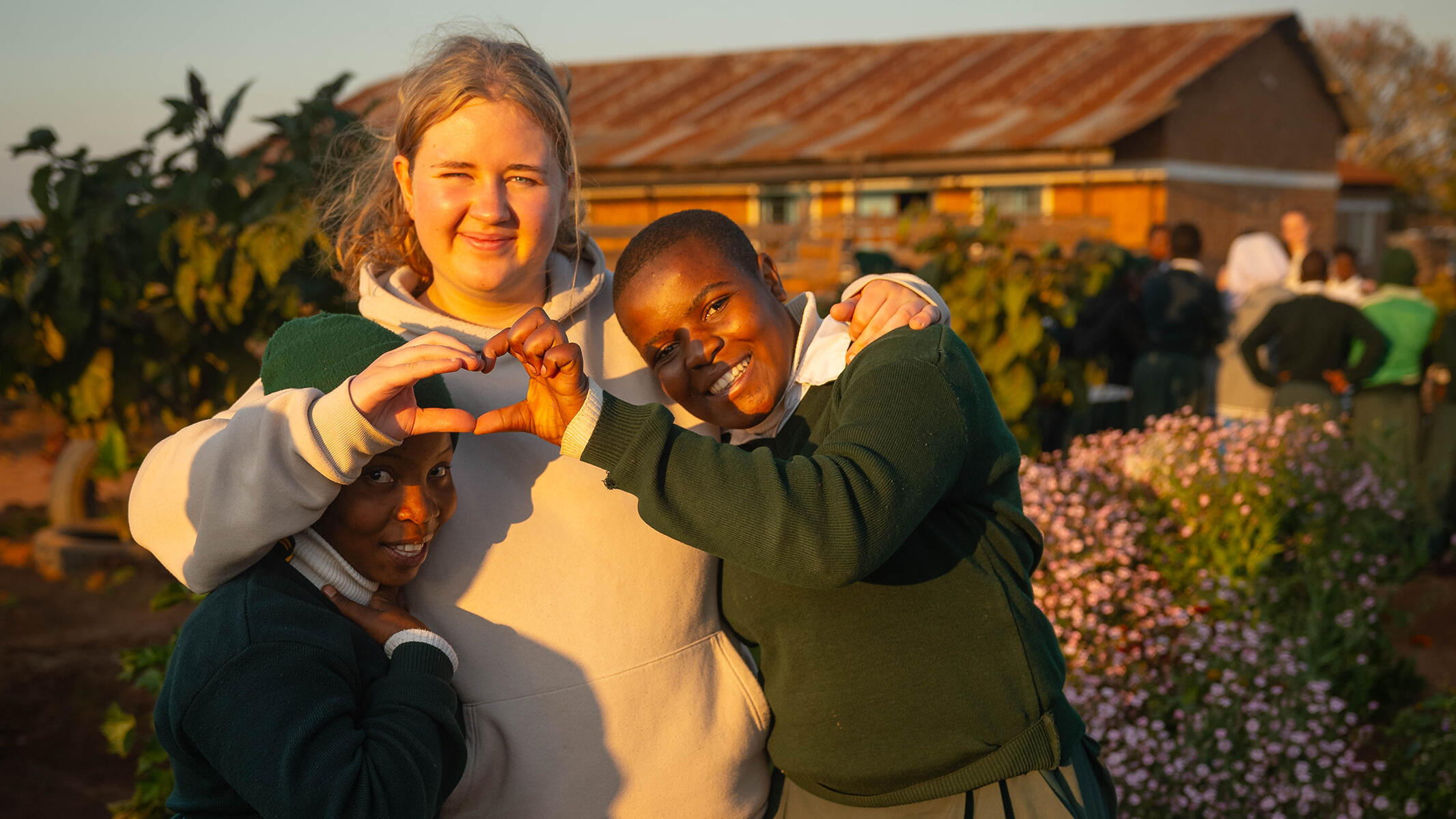 Drei Schülerinnen aus Gräfelfing und Emmaberg posieren gemeinsam. Eine deutsche und eine tansanische Schülerin formen mit ihren Händen gemeinsam ein Herz.