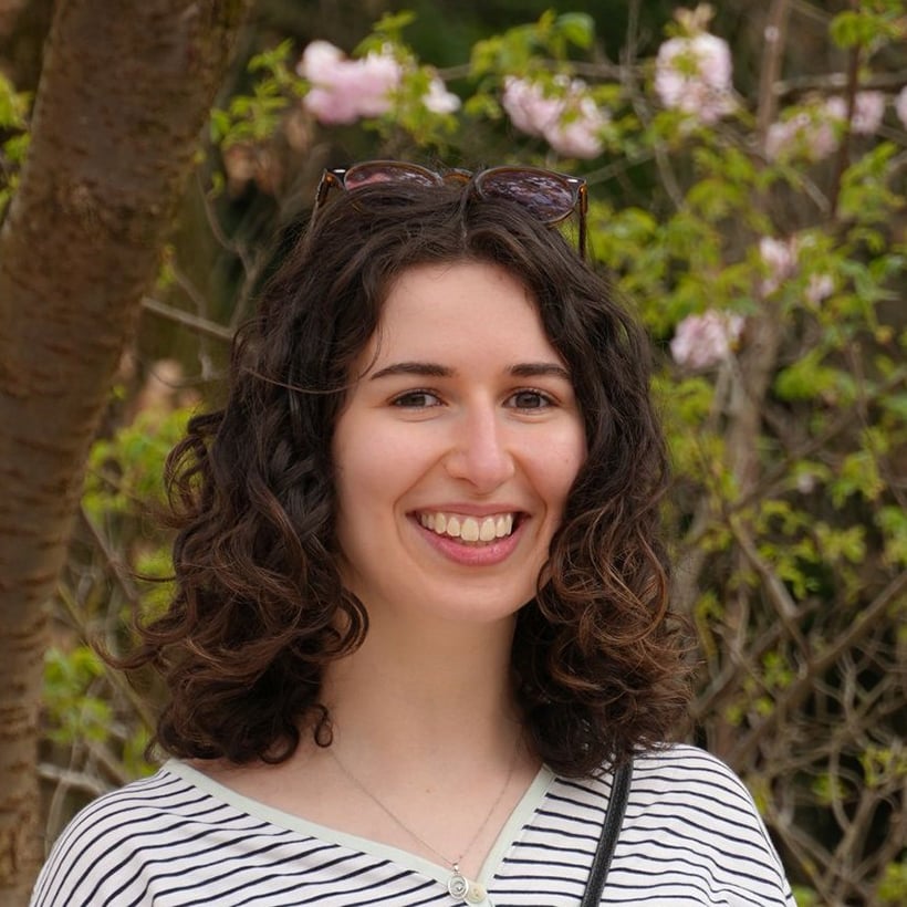 YFU-Ehrenamtliche Israa Kretschmer vor einer Landschaft mit Bäumen und rosa Blüten mit Sonnenbrille auf dem Kopf