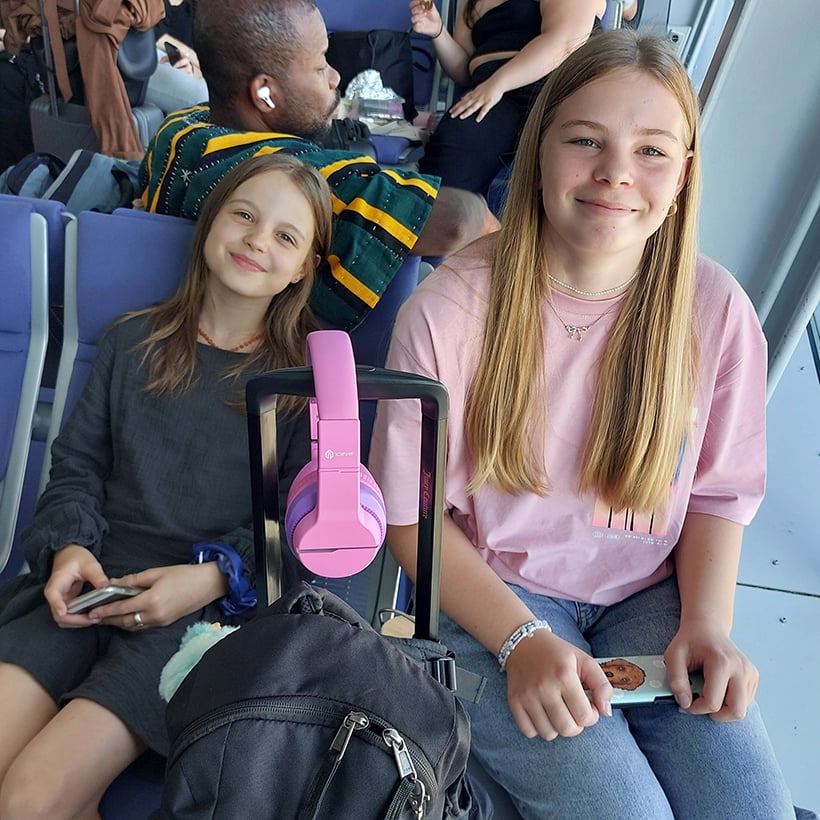 Die Mittelschülerinnen Philia und Ida sitzen abflugbereit am Flughafen, zwischen ihnen steht ein Koffer